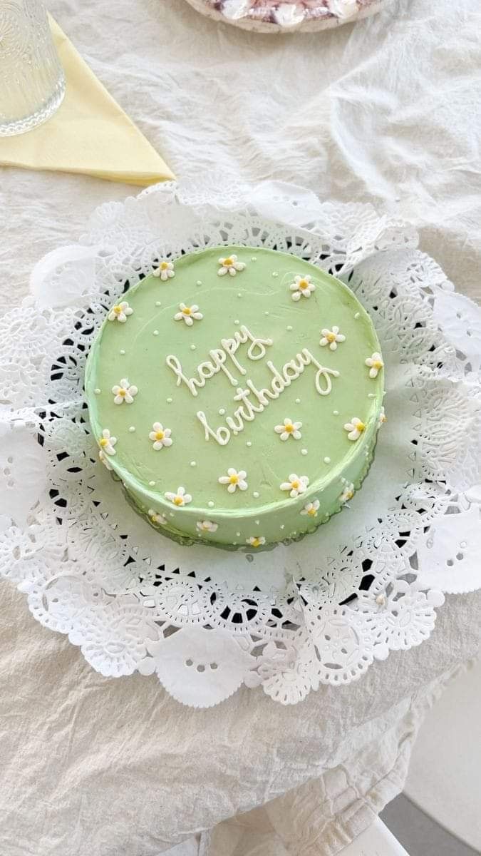 a green cake sitting on top of a white doily next to a plate with flowers