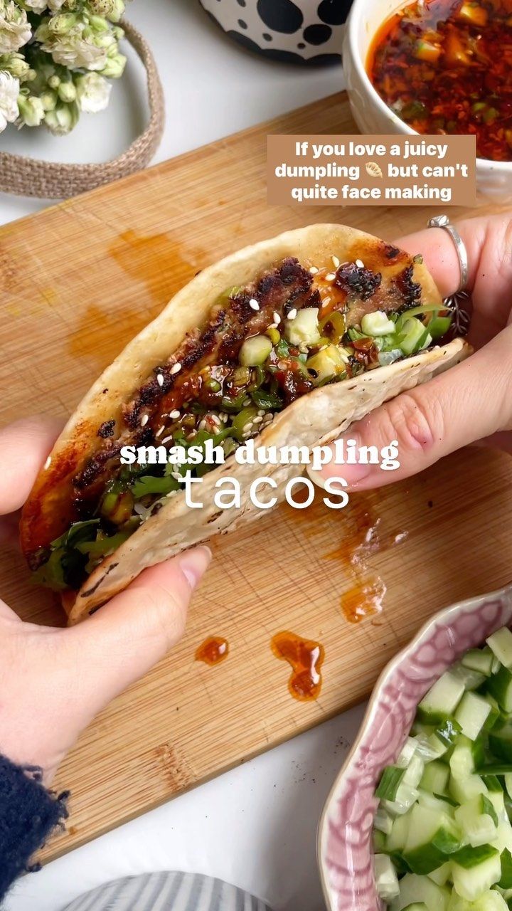 a person holding a taco in their hand next to bowls of vegetables and sauces