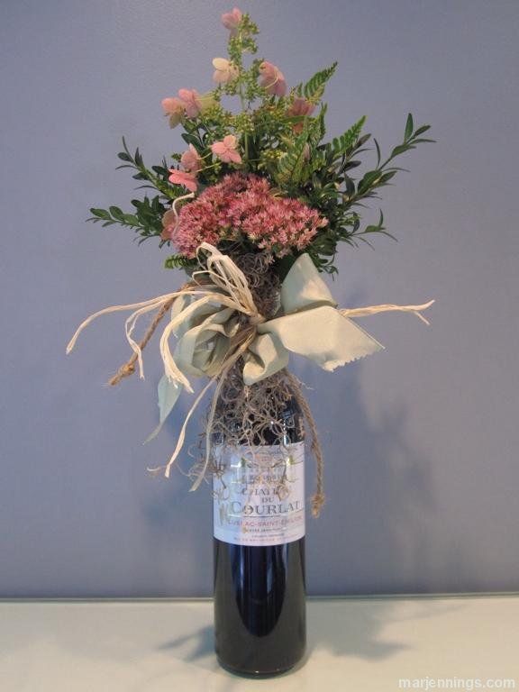 a wine bottle with flowers in it sitting on a table next to a gray wall