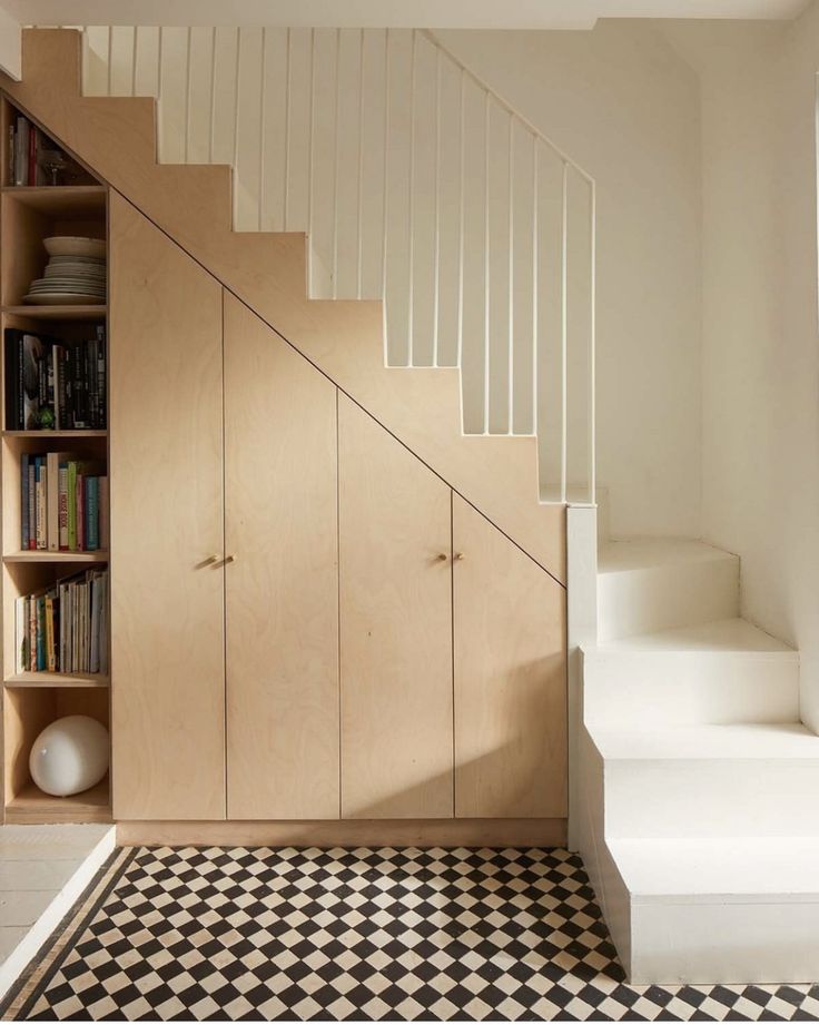 a white staircase with bookshelves next to a black and white checkered floor