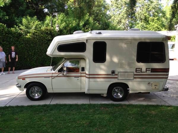 an rv is parked on the side of the road with people walking in the background