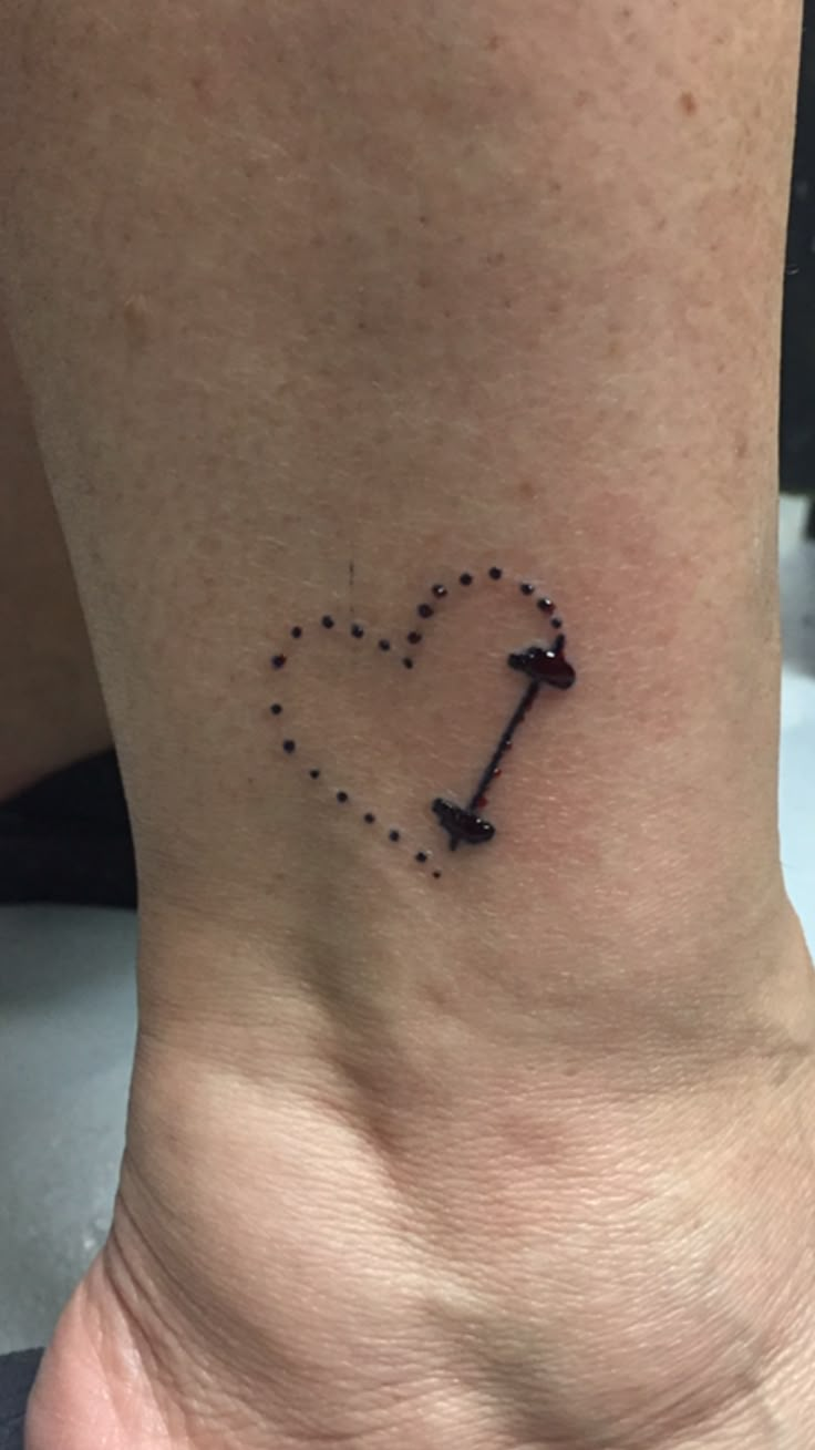 a small tattoo on the ankle of a woman with an arrow in the shape of a heart