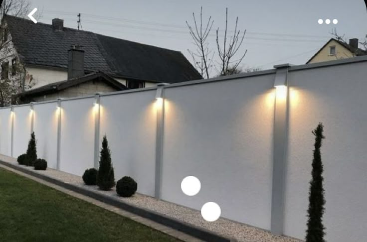 a white fence with lights on it and some bushes in the foreground next to it