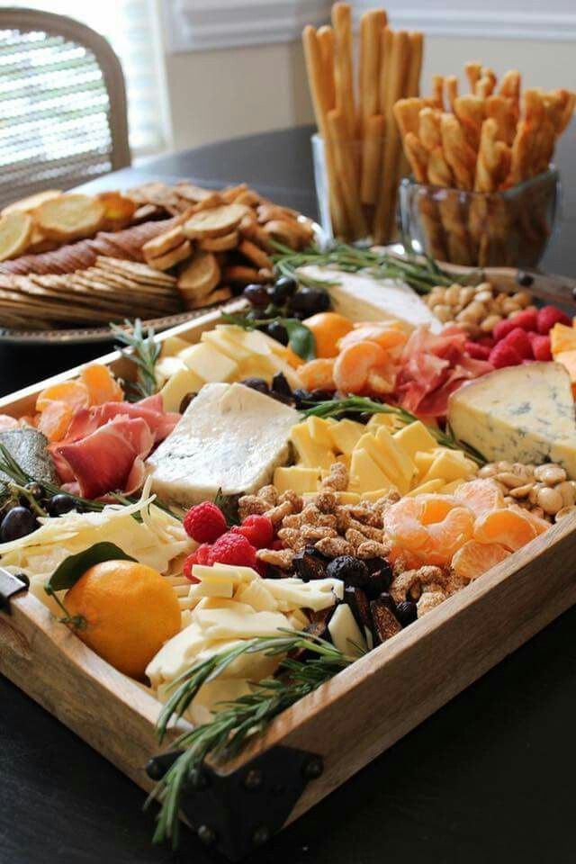 an assortment of cheeses, crackers and fruit on a wooden tray with other snacks