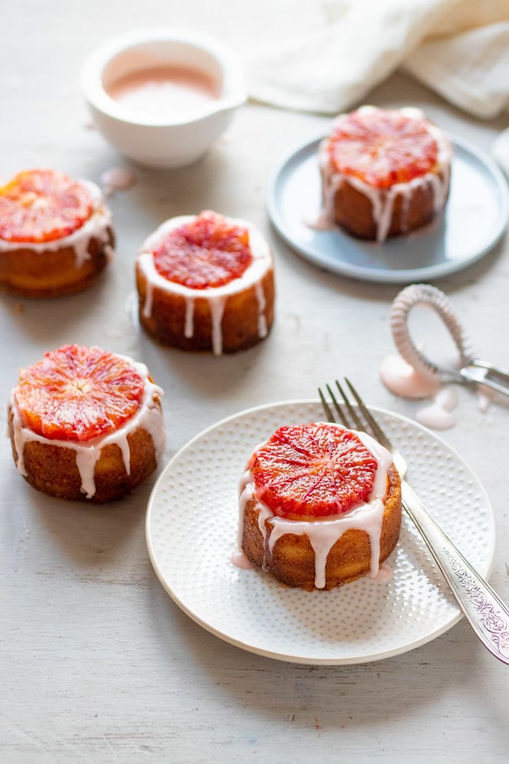 blood orange buns with icing on a white plate next to silverware and utensils