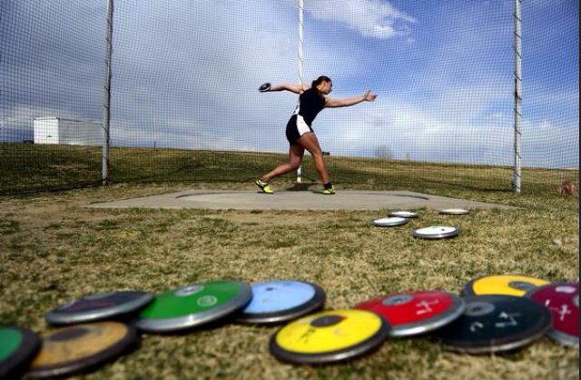 a woman throwing a frisbee on top of a grass covered field next to a fence