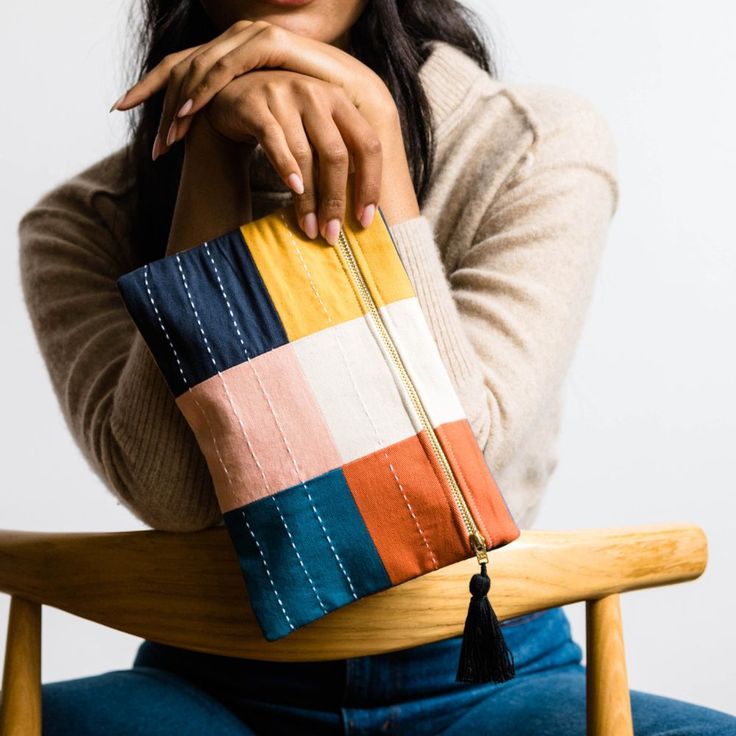 a woman sitting in a chair holding a multicolored purse with one hand on her shoulder