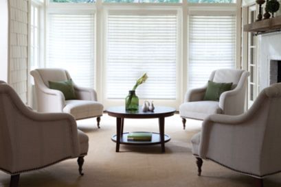 a living room with two chairs and a table in front of large windows that have blinds on them