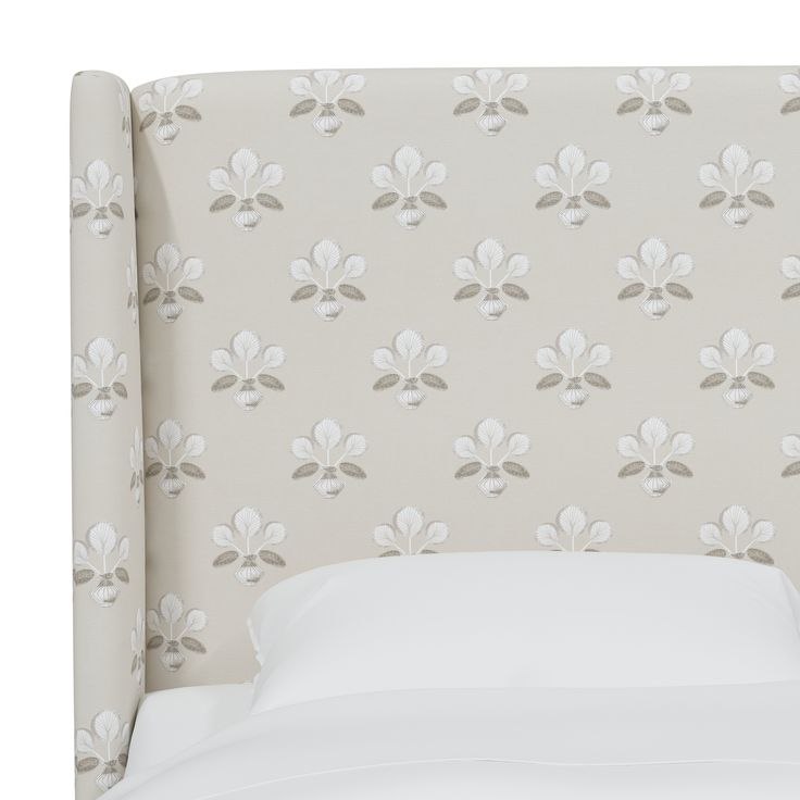 an upholstered headboard with white and gray flowers on the wall behind it