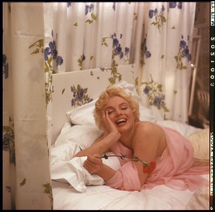 a woman laying on top of a bed in a pink dress with her hand under her chin