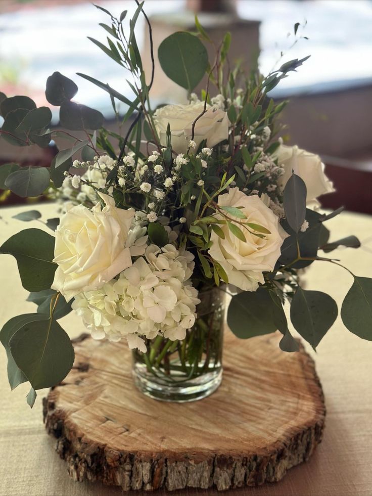 a vase filled with white flowers sitting on top of a wooden slice