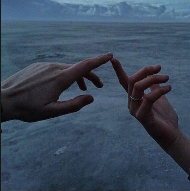 two hands reaching out towards each other in front of an ocean with mountains and clouds