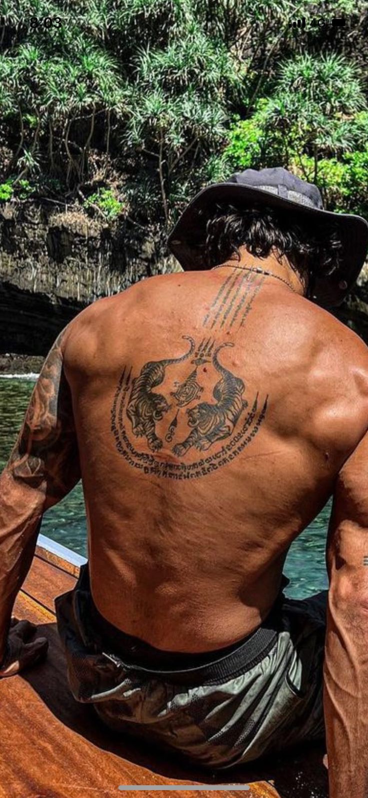 a man sitting on top of a boat in the water with tattoos on his back