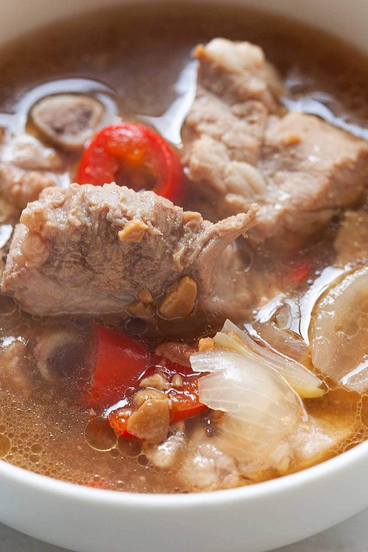 a white bowl filled with meat and vegetables on top of a marble counter next to a red pepper