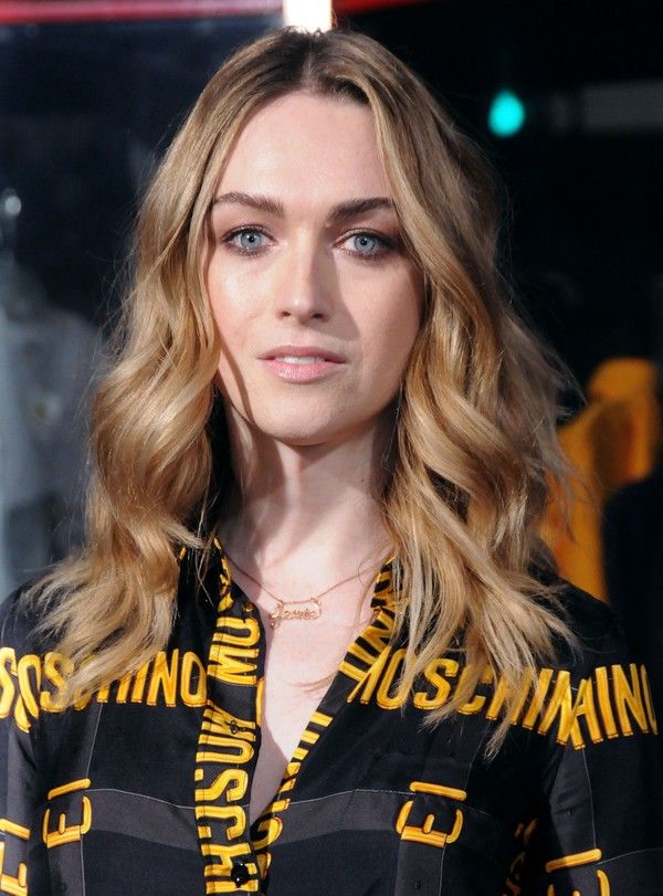 a woman with blonde hair and blue eyes wearing a black shirt that has yellow letters on it