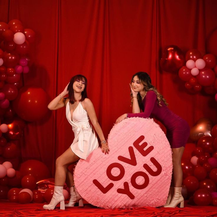 two women posing in front of a giant heart shaped pillow with the word love on it