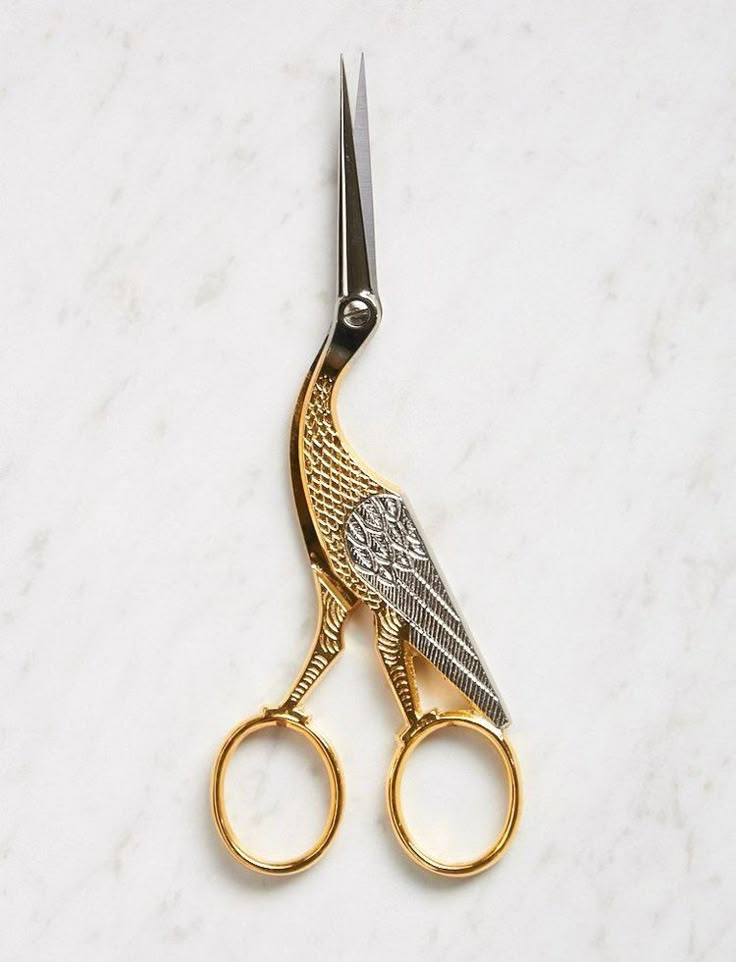 a pair of gold scissors on a white marble counter top with an angel wing design