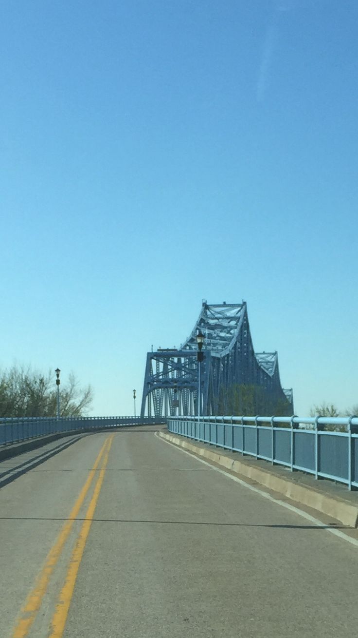 an empty highway with a blue bridge in the back ground and trees on either side