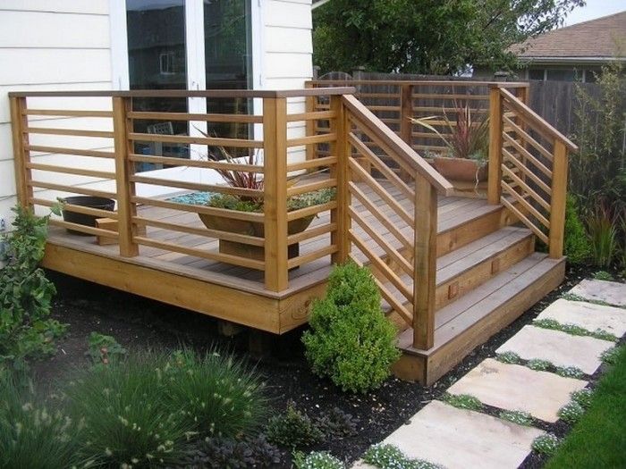 a wooden deck in front of a house with plants on it and steps leading up to the door