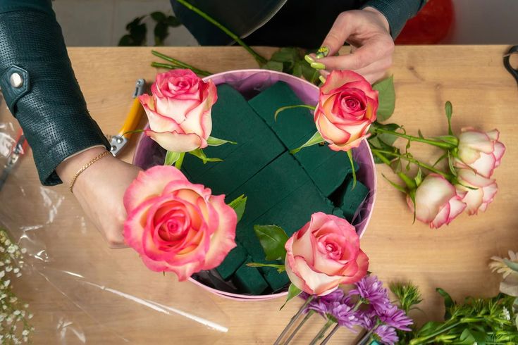 a person arranging flowers on a table with scissors and cutting them into squares in the shape of a heart