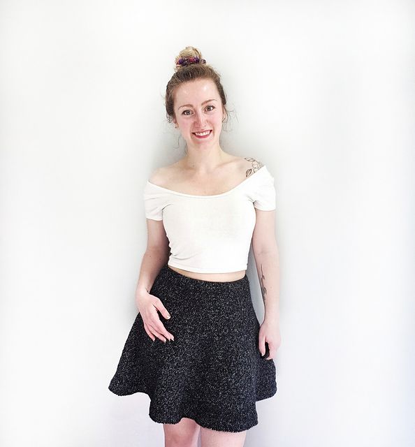 a woman standing in front of a white wall wearing a black skirt and crop top