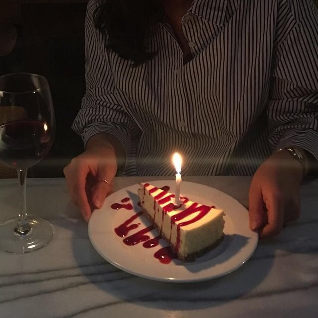 a woman sitting at a table with a slice of cake on it and a lit candle in front of her