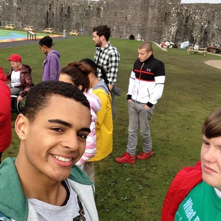 a group of people standing around each other on a grass covered field with a castle in the background