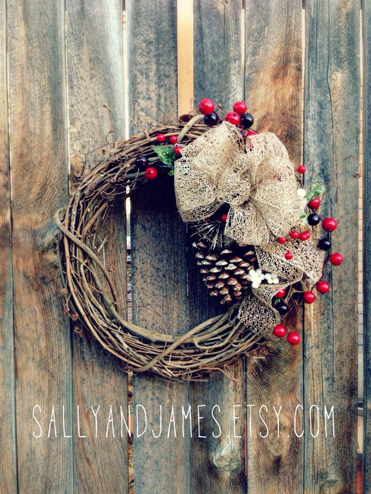 a wreath with red berries and pine cones hanging on the side of a wooden fence