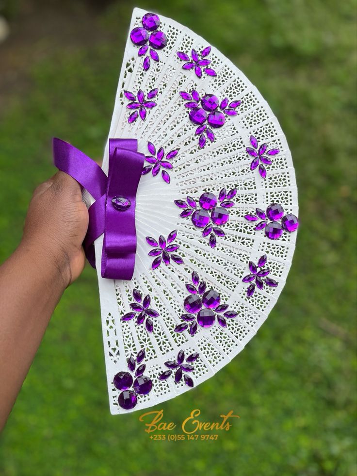 a hand holding an umbrella with purple flowers on it and a ribbon around the handle