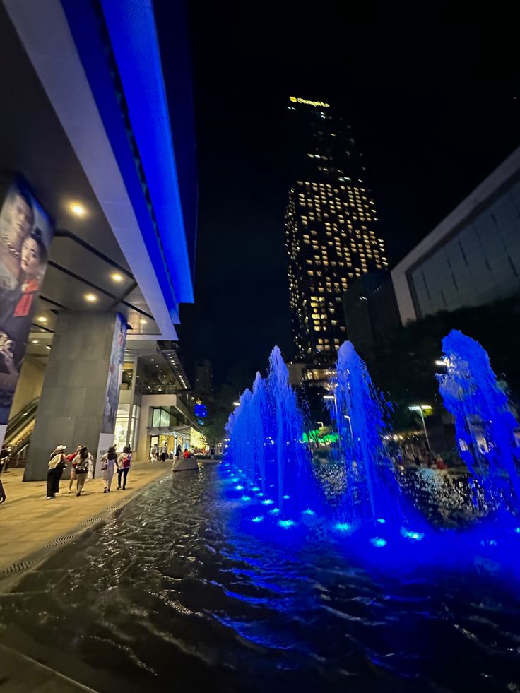 blue lights are shining on the water fountain in front of a tall building at night