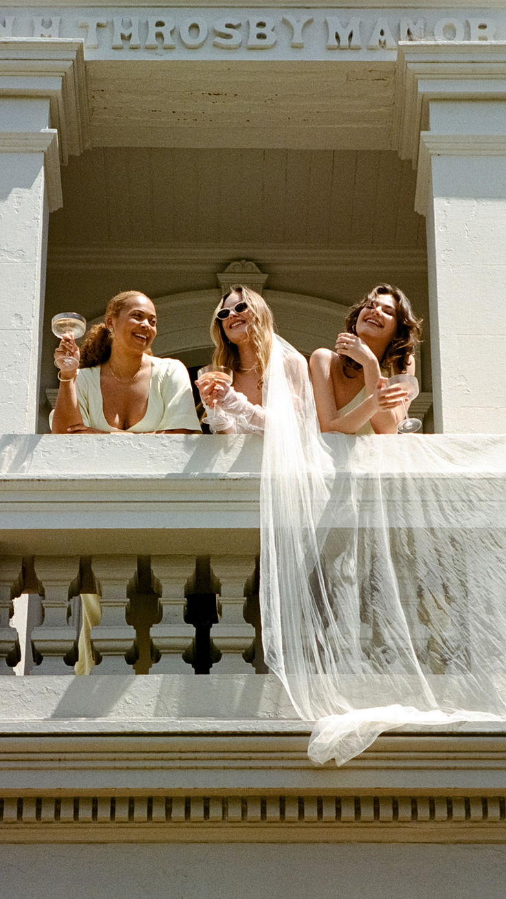 three women standing on a balcony holding wine glasses