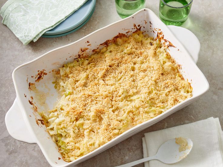 a casserole dish on a table with two glasses and napkins next to it