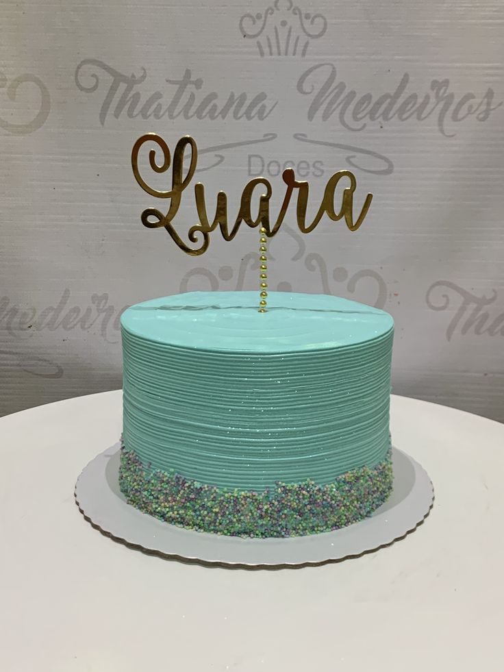 a blue cake with the word luara on top is sitting on a white table