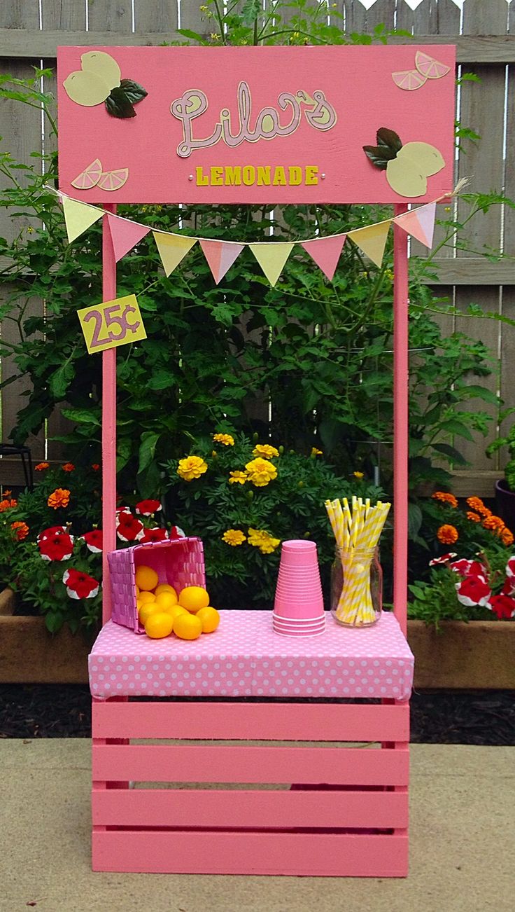 a pink lemonade stand in front of some flowers