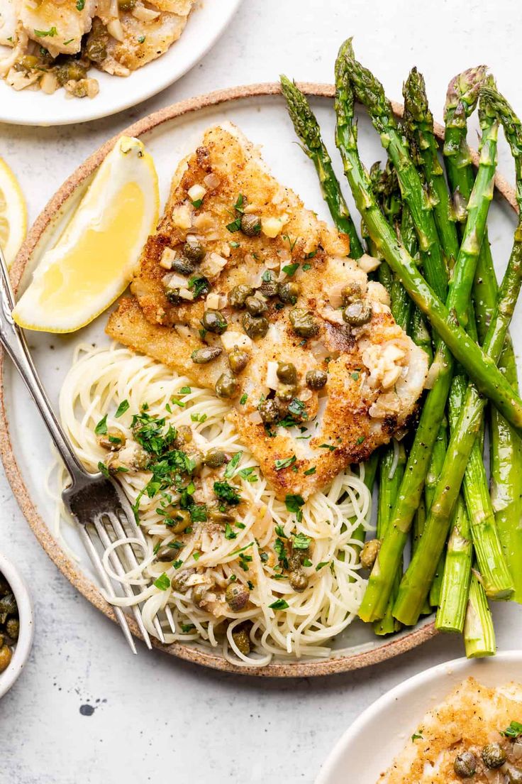 a plate with chicken, pasta and asparagus on it next to lemon wedges