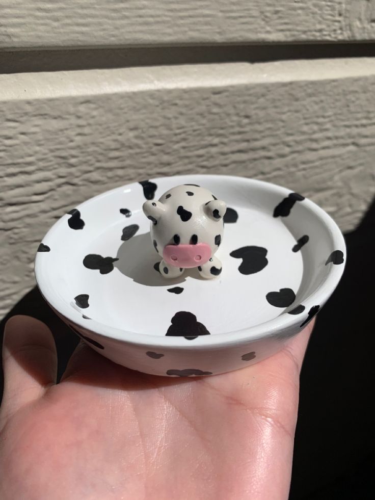 a small cow figurine sitting on top of a white bowl in someone's hand