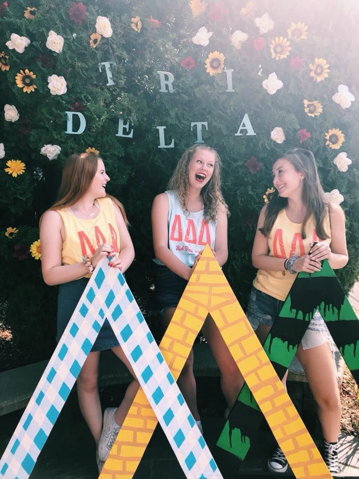 three girls are standing in front of a wall decorated with flowers and letters that spell out the word delta