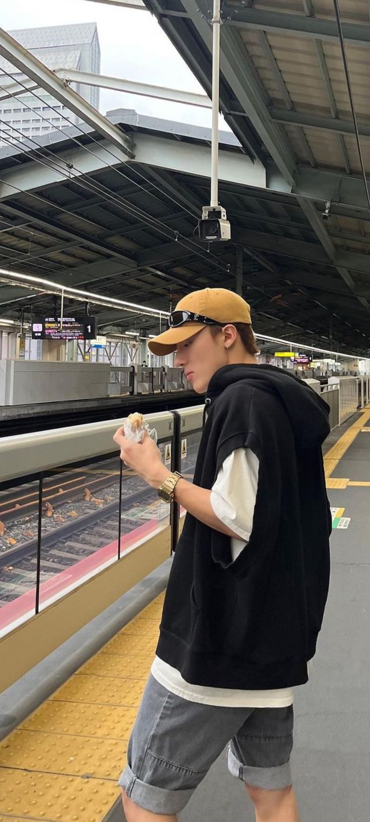 a man standing on a train platform looking at his cell phone and wearing a hat