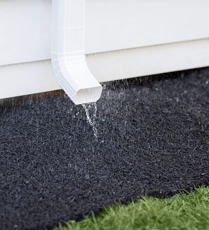 water coming out of the gutter into a black area next to a white house