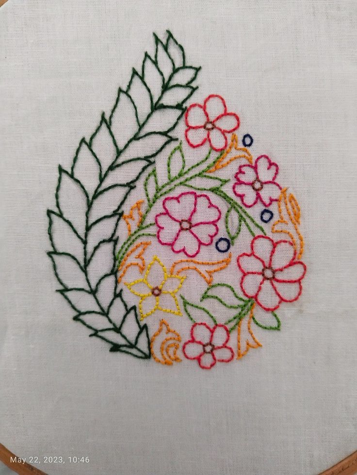 a close up of a embroidery on a piece of cloth with leaves and flowers in the center