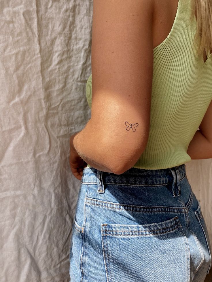 a woman with a small butterfly tattoo on her left arm, standing in front of a white sheet