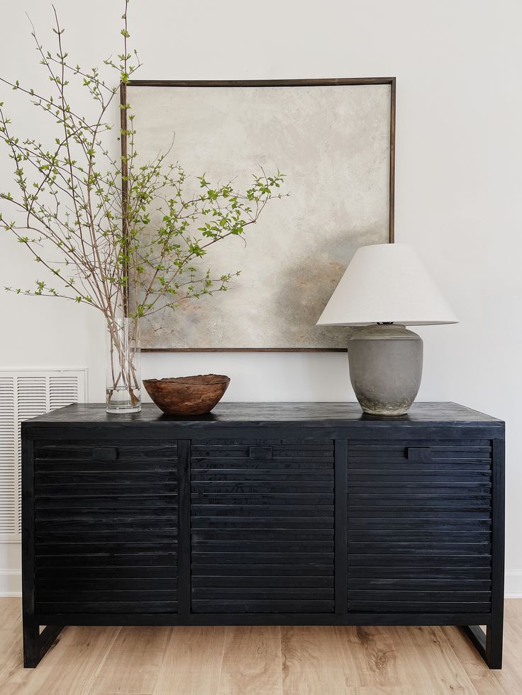 a black cabinet with two vases and a lamp next to it on a hard wood floor