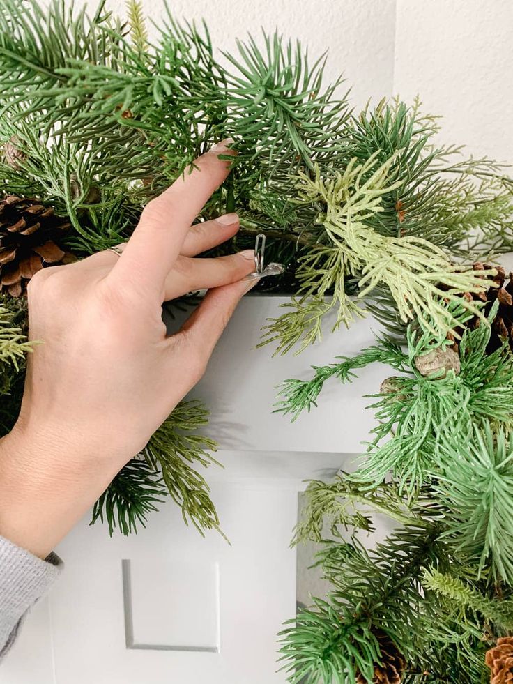 a person is placing pine cones on the top of a christmas wreath with evergreen needles