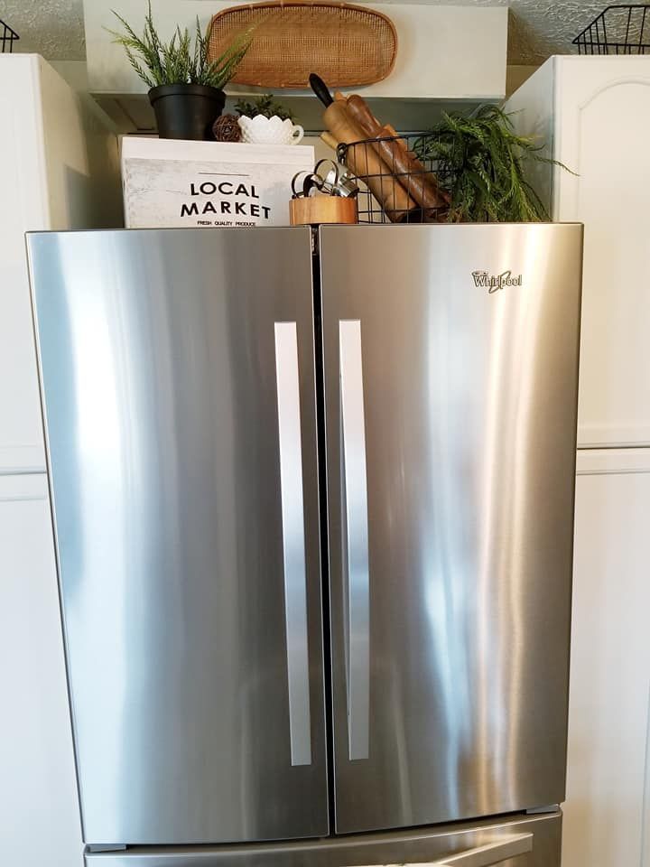 a stainless steel refrigerator in a kitchen next to white cabinets and cupboards with baskets on top