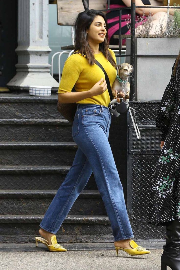 a woman walking down the street carrying a small dog in her hand and wearing high heeled shoes