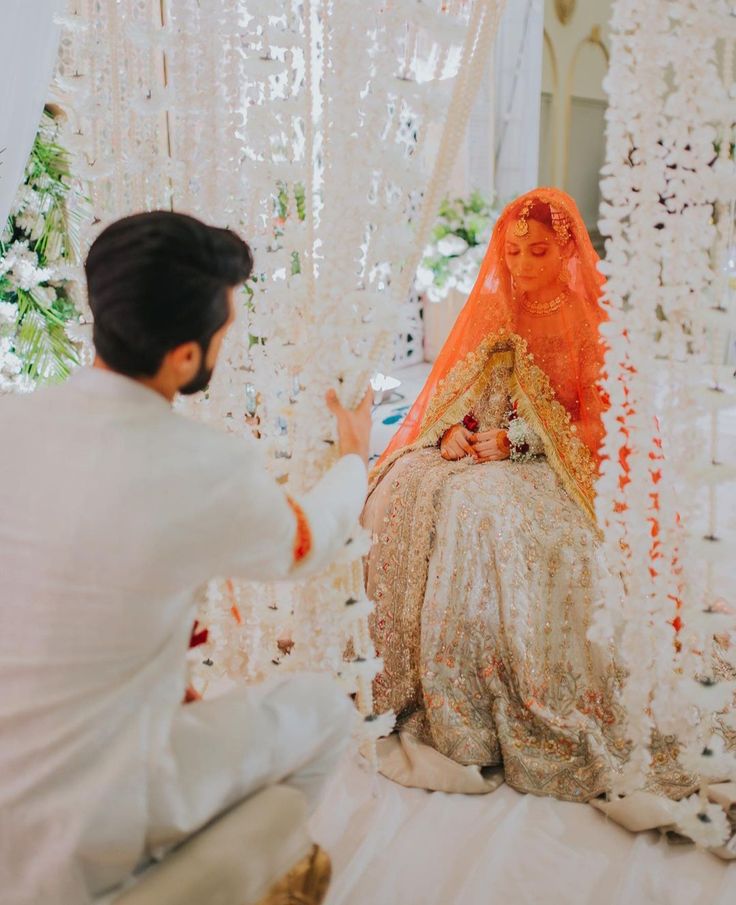 a man kneeling down next to a woman in a white dress and orange shawl