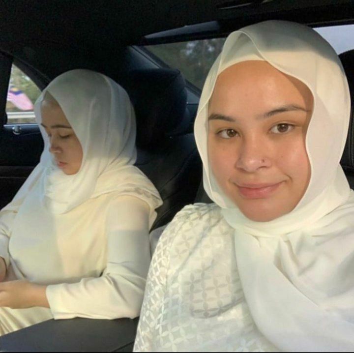 two women sitting in the back seat of a car, both wearing headscarves