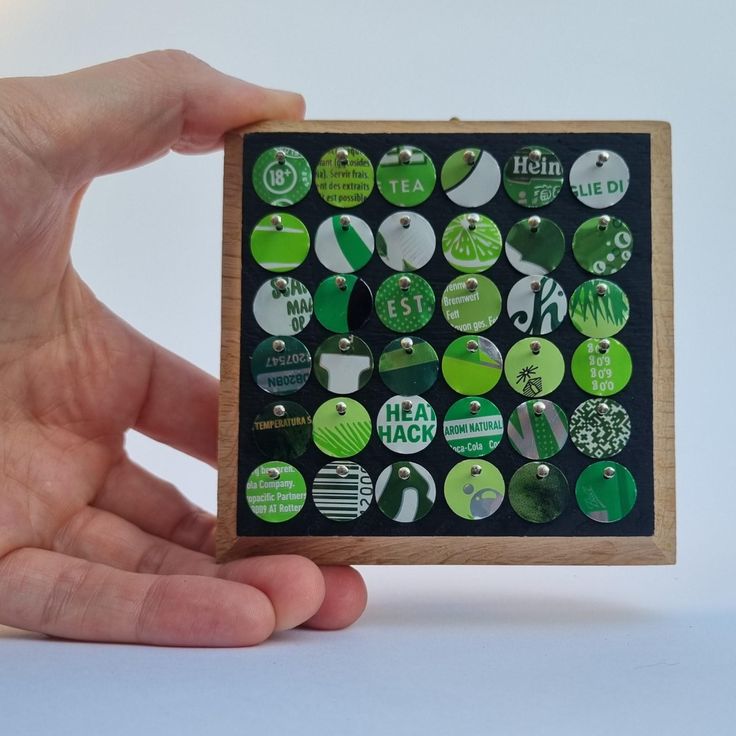 a person holding up a wooden frame with green and white buttons on it