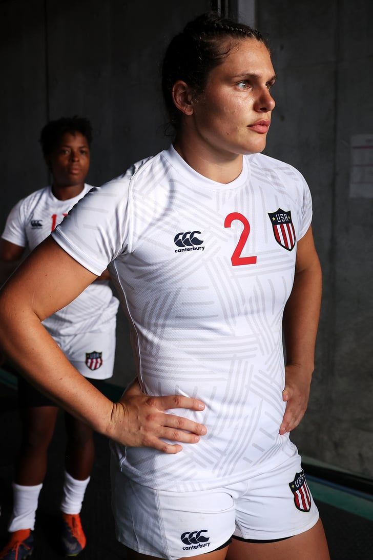 two female rugby players are posing for a photo in their uniforms, one is holding her stomach and the other has her hands on her hips