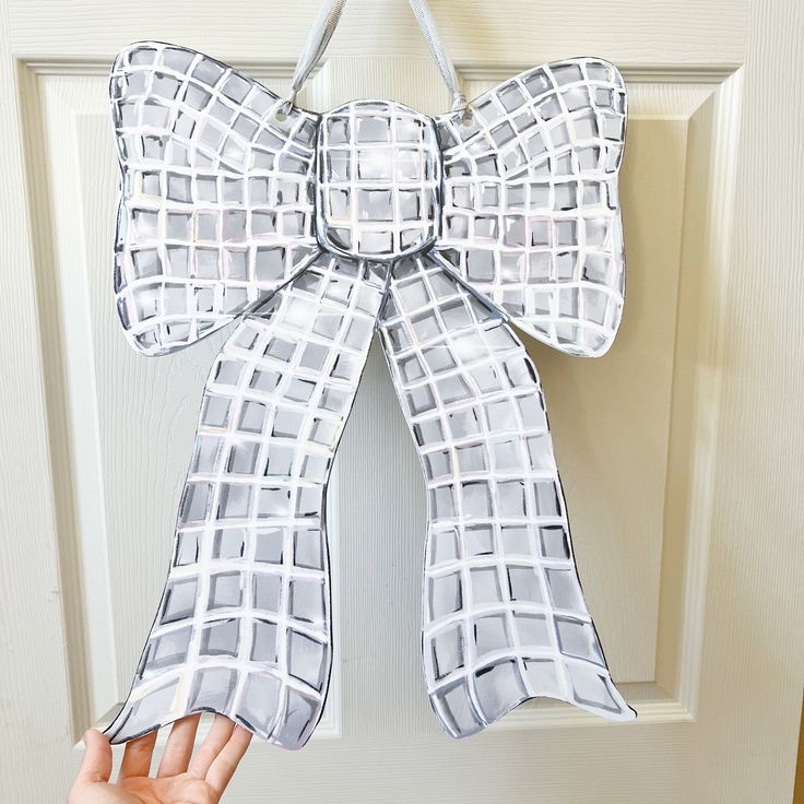 a hand is holding up a paper bow on the front door to show it's size